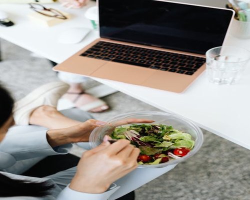Persona trabajando en laptop y comiendo ensalada